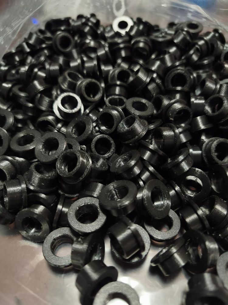 Una bolsa con cientos de bujes negros con pestaña, impresos en 3D